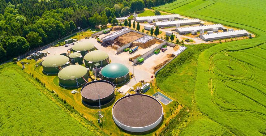 Aerial view over biogas plant and farm in green fields