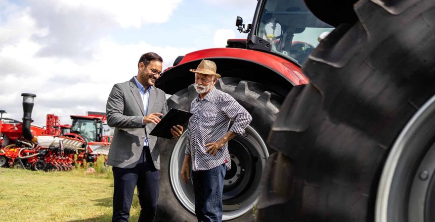 Two people discussing loans in front of tractors
